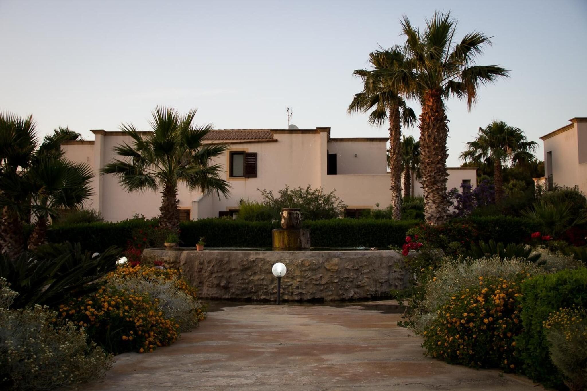 A residential area with modern houses, palm trees, and a stone wall with a spherical light fixture.