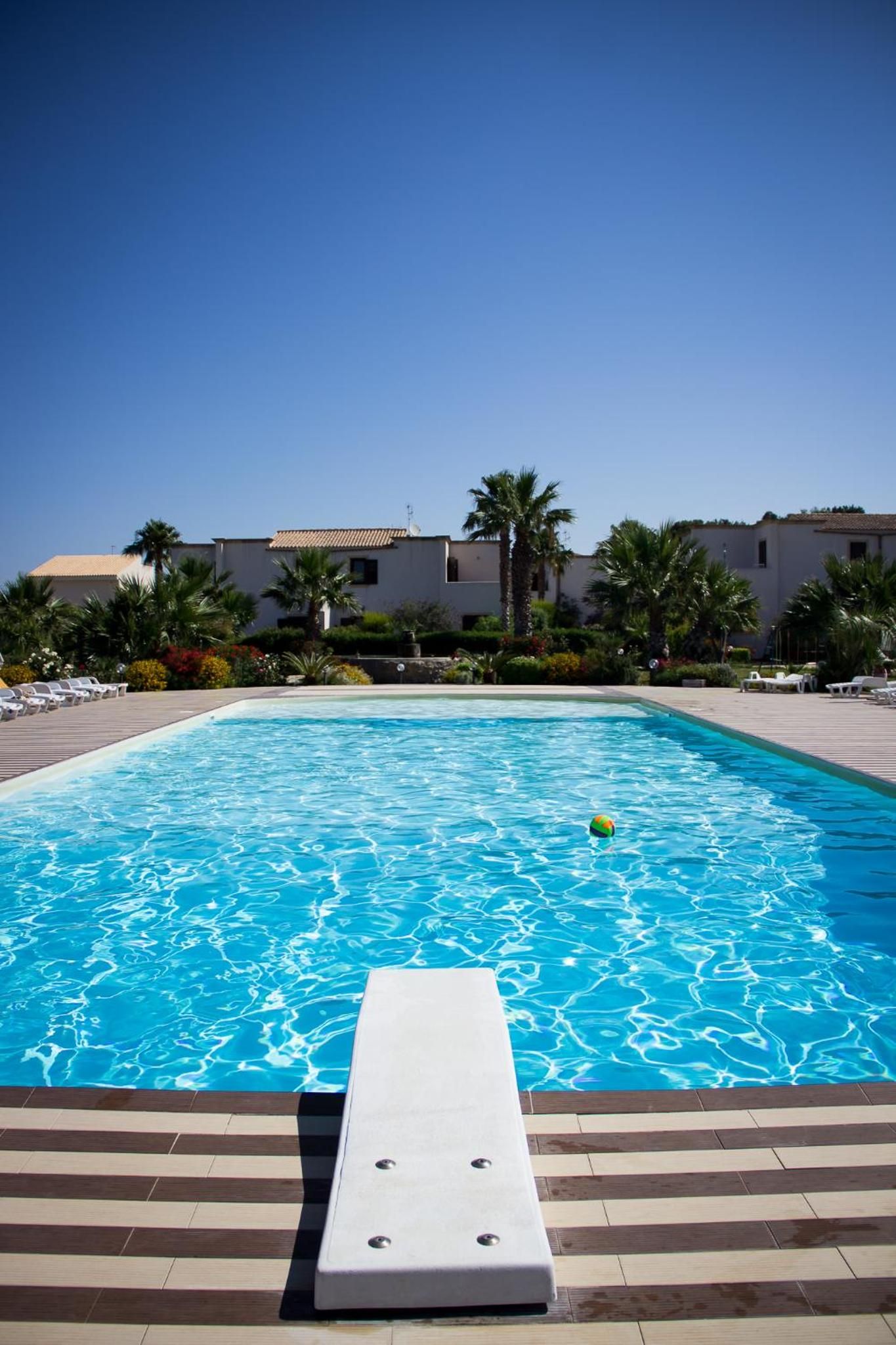 Une piscine avec un espace de détente, des palmiers et des bâtiments en arrière-plan.