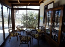 Una veranda riparata con mobili in vimini e un tavolo in vetro, con vista su un giardino e una strada.