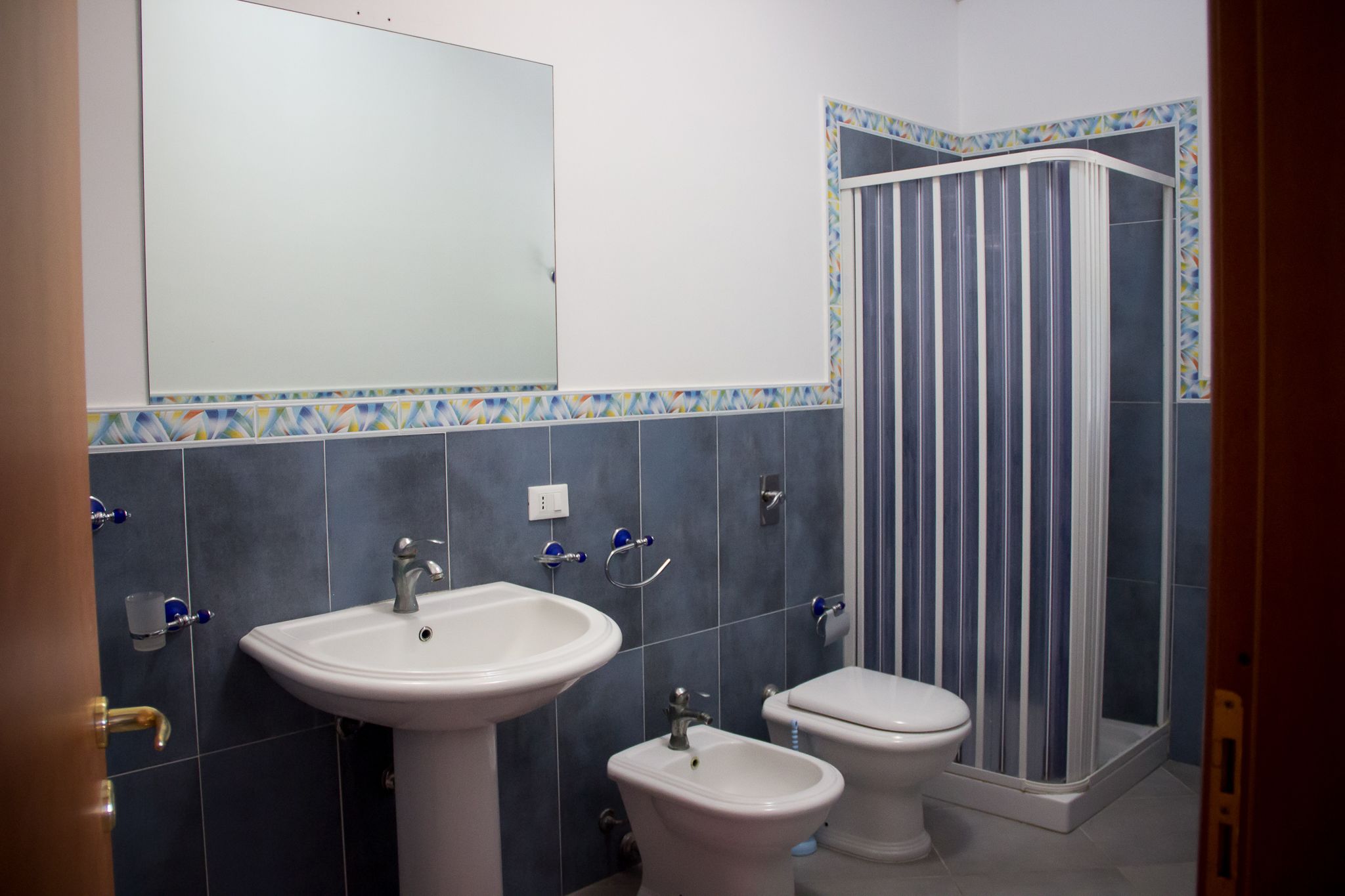 Un baño con lavamanos, bidé, inodoro y ducha con cortina a rayas.