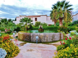 Un cortile con una fontana, circondato da piante rigogliose e fiori.