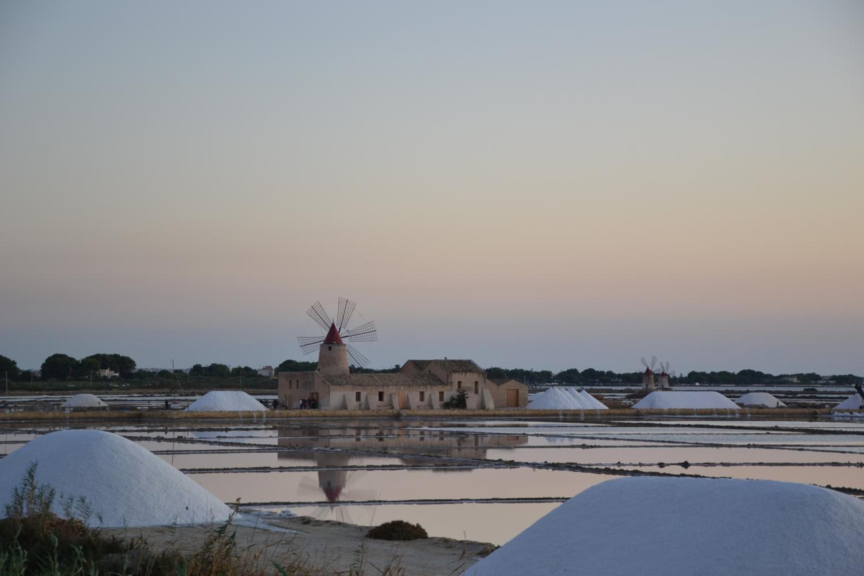 A windmill with a traditional design, surrounded by agricultural fields and water bodies.