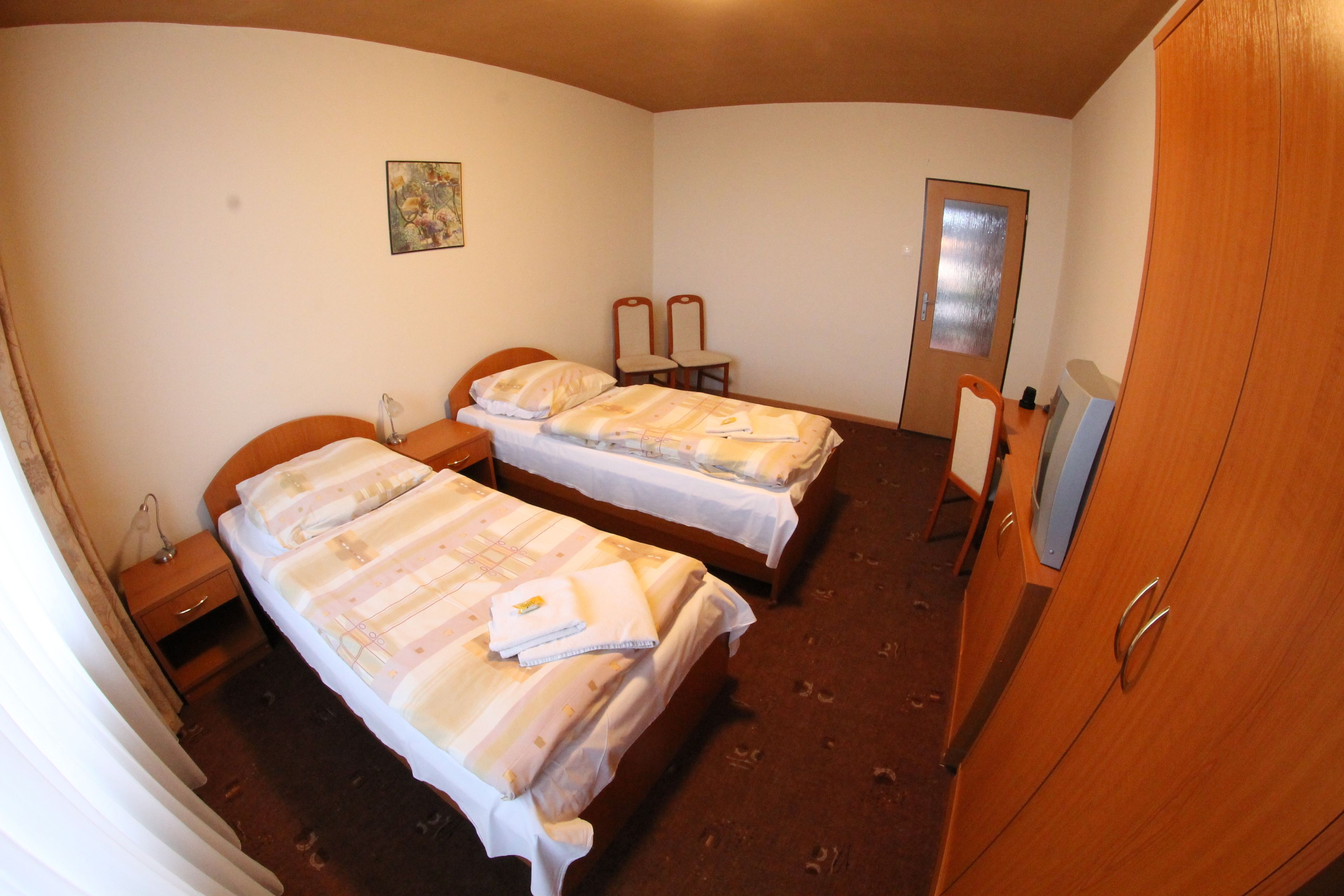 Una habitación con dos camas, un armario de madera, un escritorio con lámpara y un espejo.