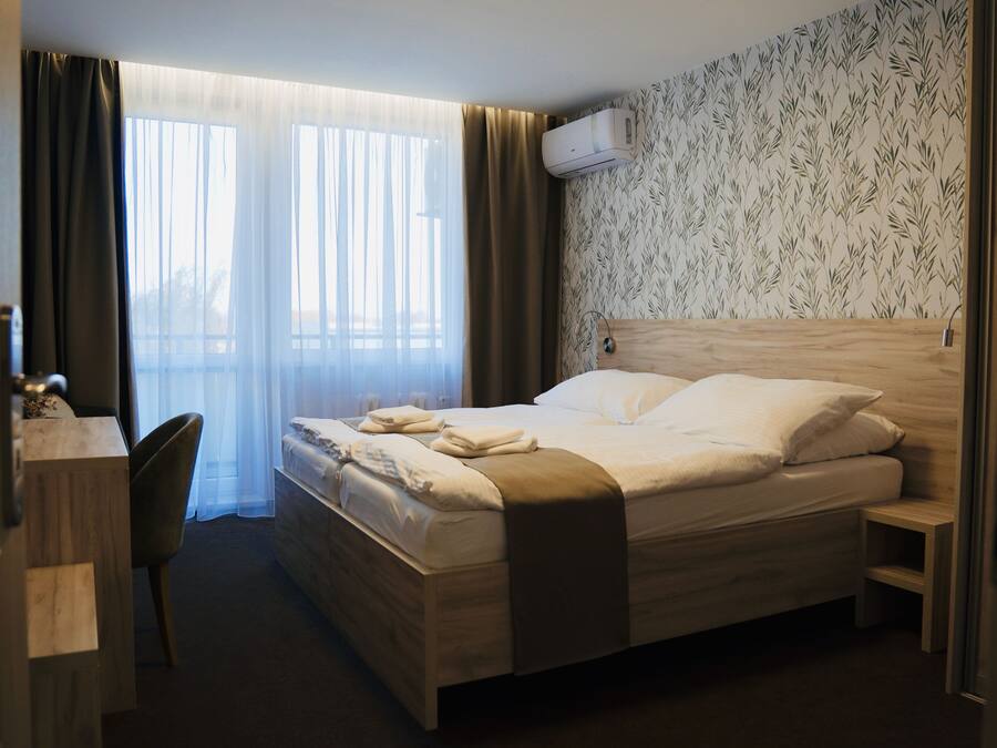 Quarto de hotel com cama, escrivaninha, cadeira, janela com cortinas e ar-condicionado na parede.