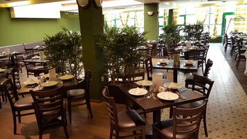 Un restaurante con varias mesas dispuestas para comer, con paredes verdes y plantas en macetas.