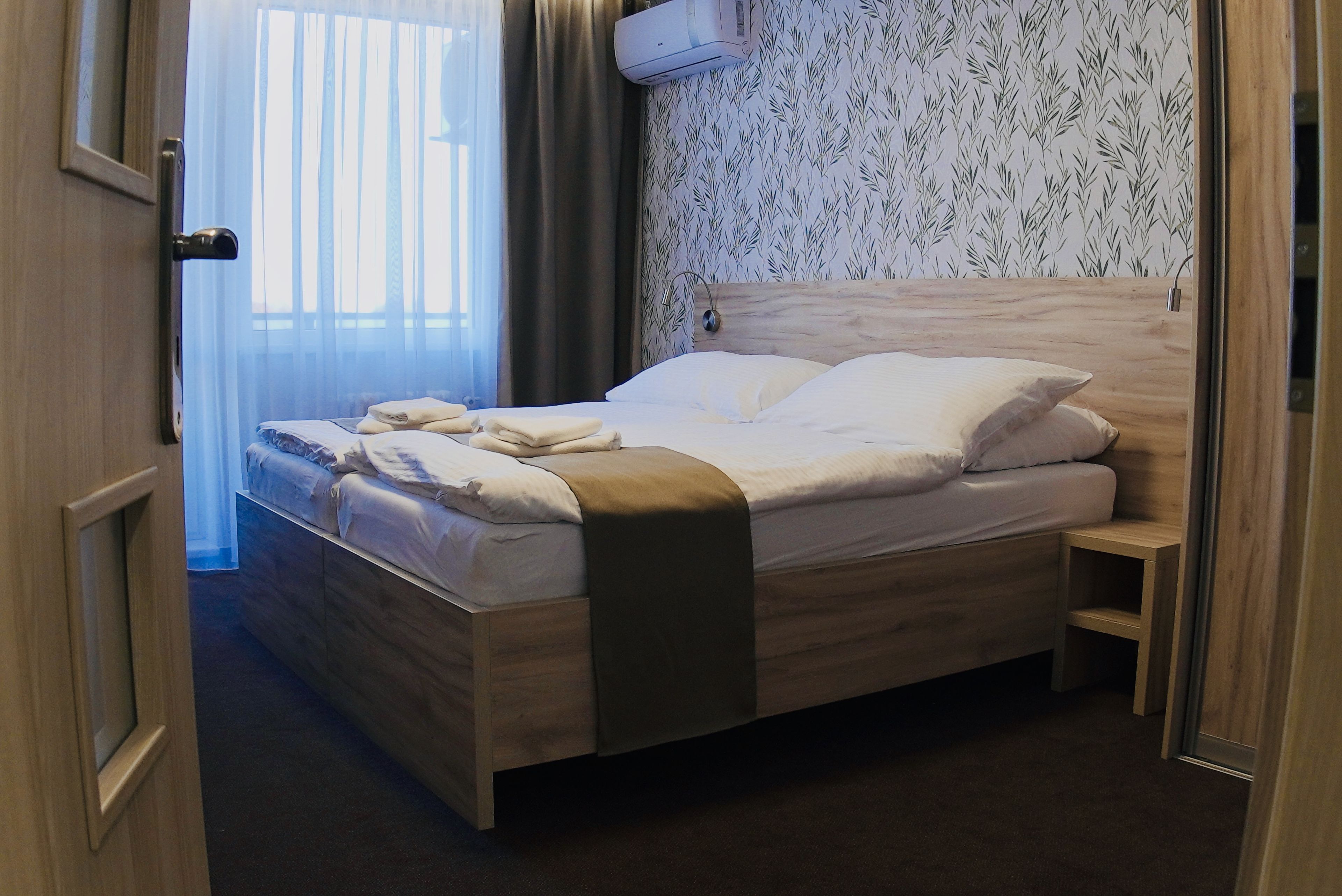 A hotel room with a wooden bed, a bedside table, and a wall-mounted air conditioner.