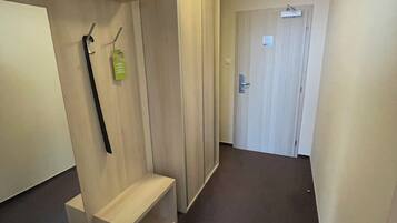A hallway with a bench, a coat rack, a door with a sign, and a light fixture.