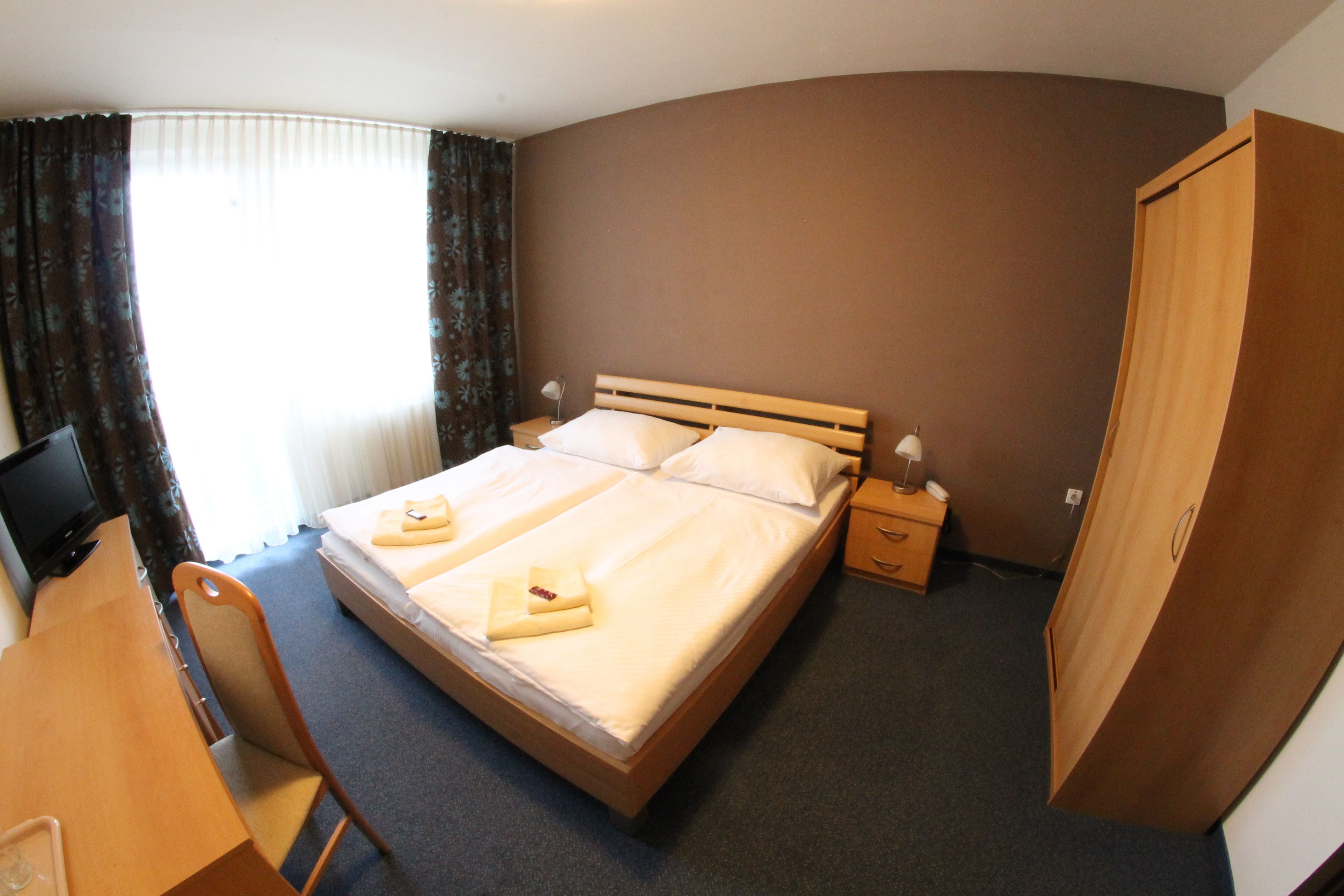 A hotel room with a bed, a desk, a chair, a wardrobe, and a television.