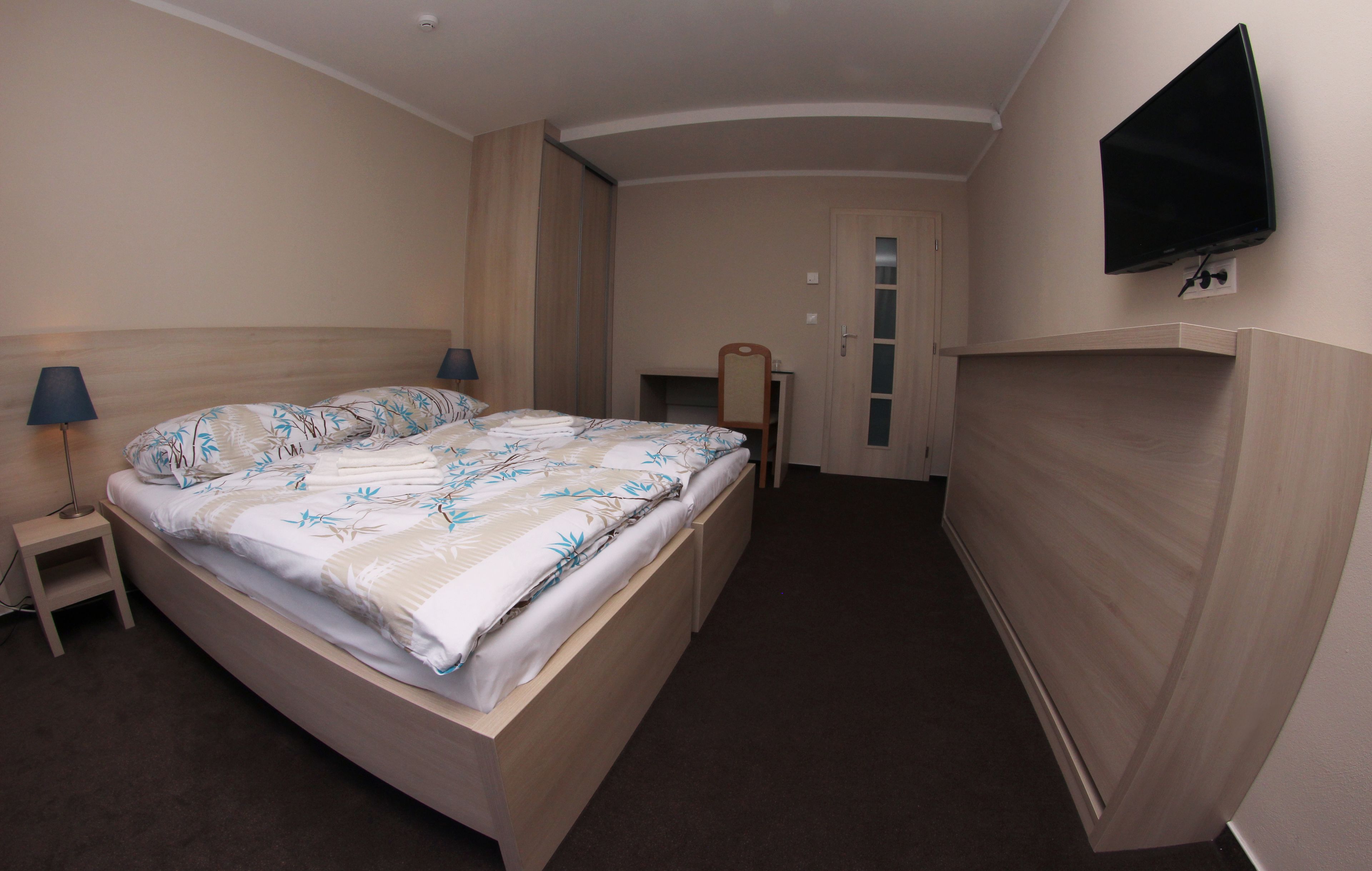 A hotel room with a bed, bedside lamps, a television, and a door.