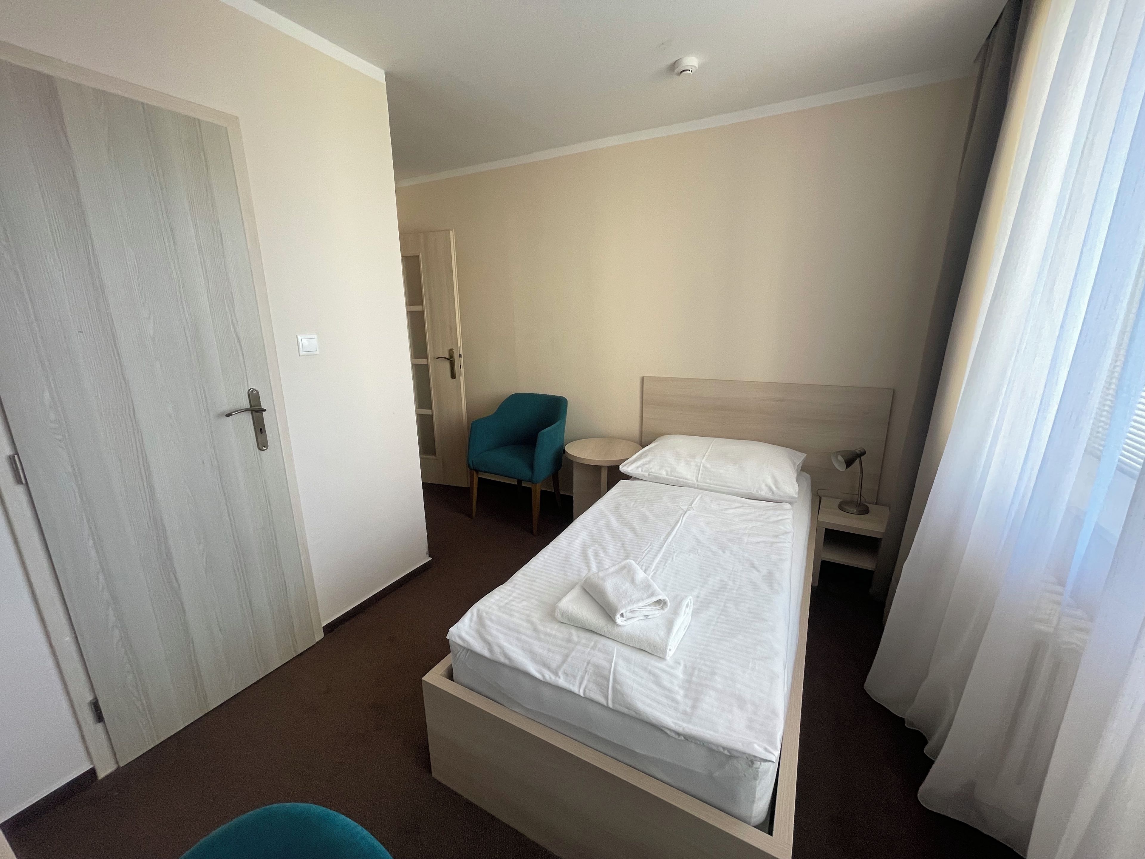 A hotel room with a bed, a chair, a bedside table, and a wardrobe.