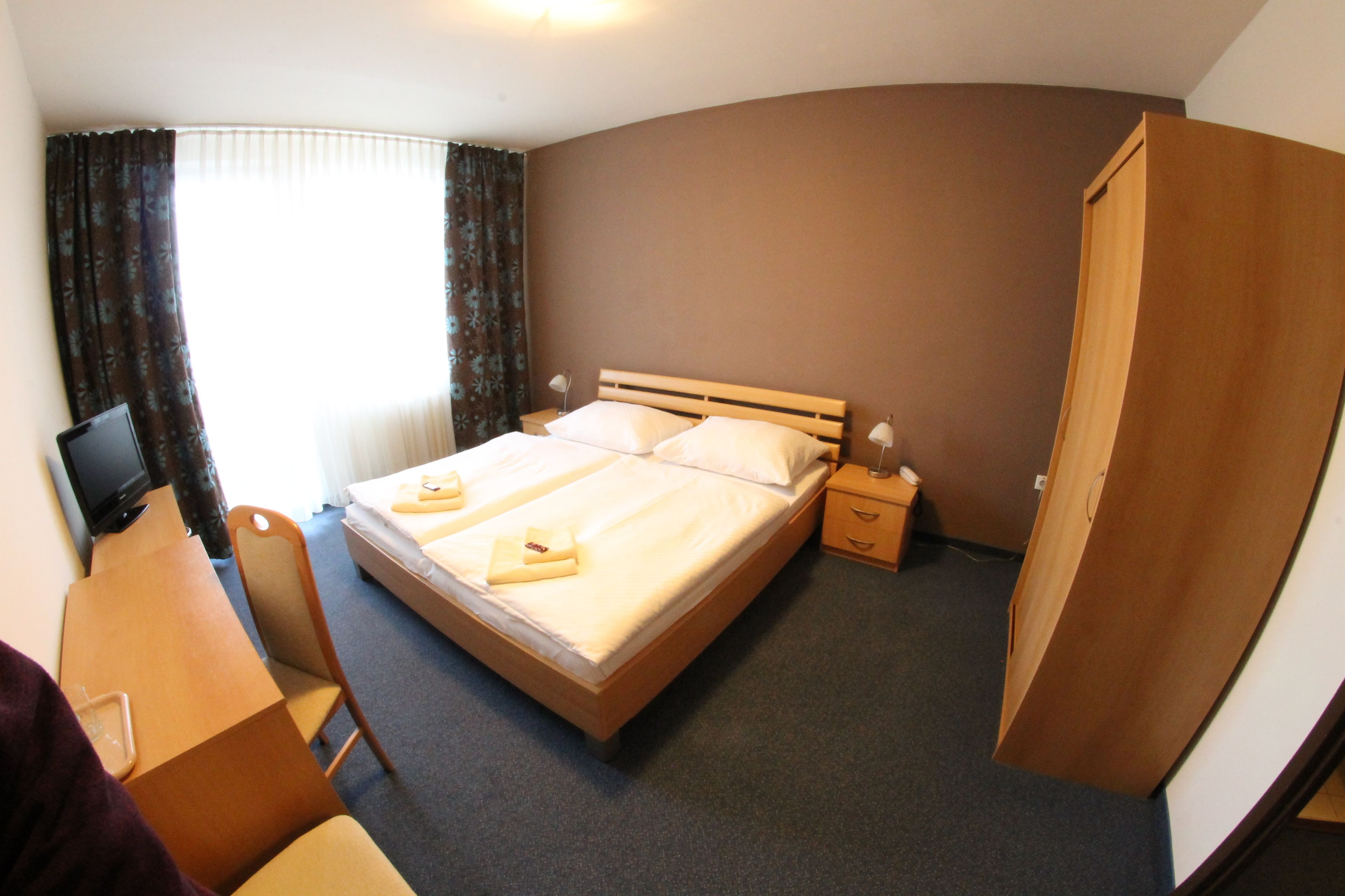 A hotel room with a bed, bedside tables, a desk, and a television.