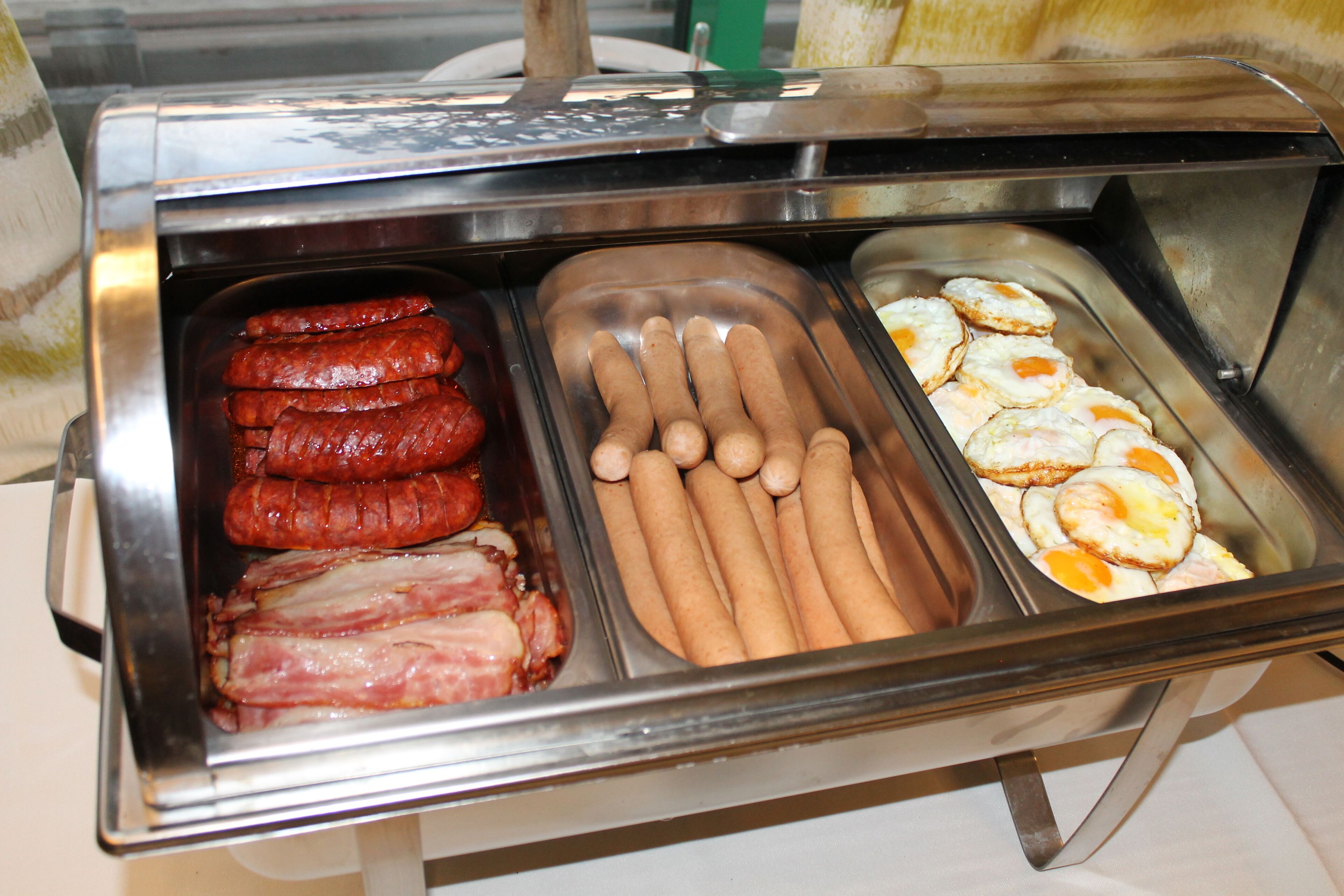 A buffet with various food items including sausages, hot dogs, and fried eggs.