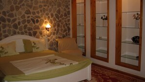 A bedroom with a stone wall, a bed with green bedding, a nightstand, and a wall-mounted shelf with decorative items. - Rem's Pension (Rasnov)