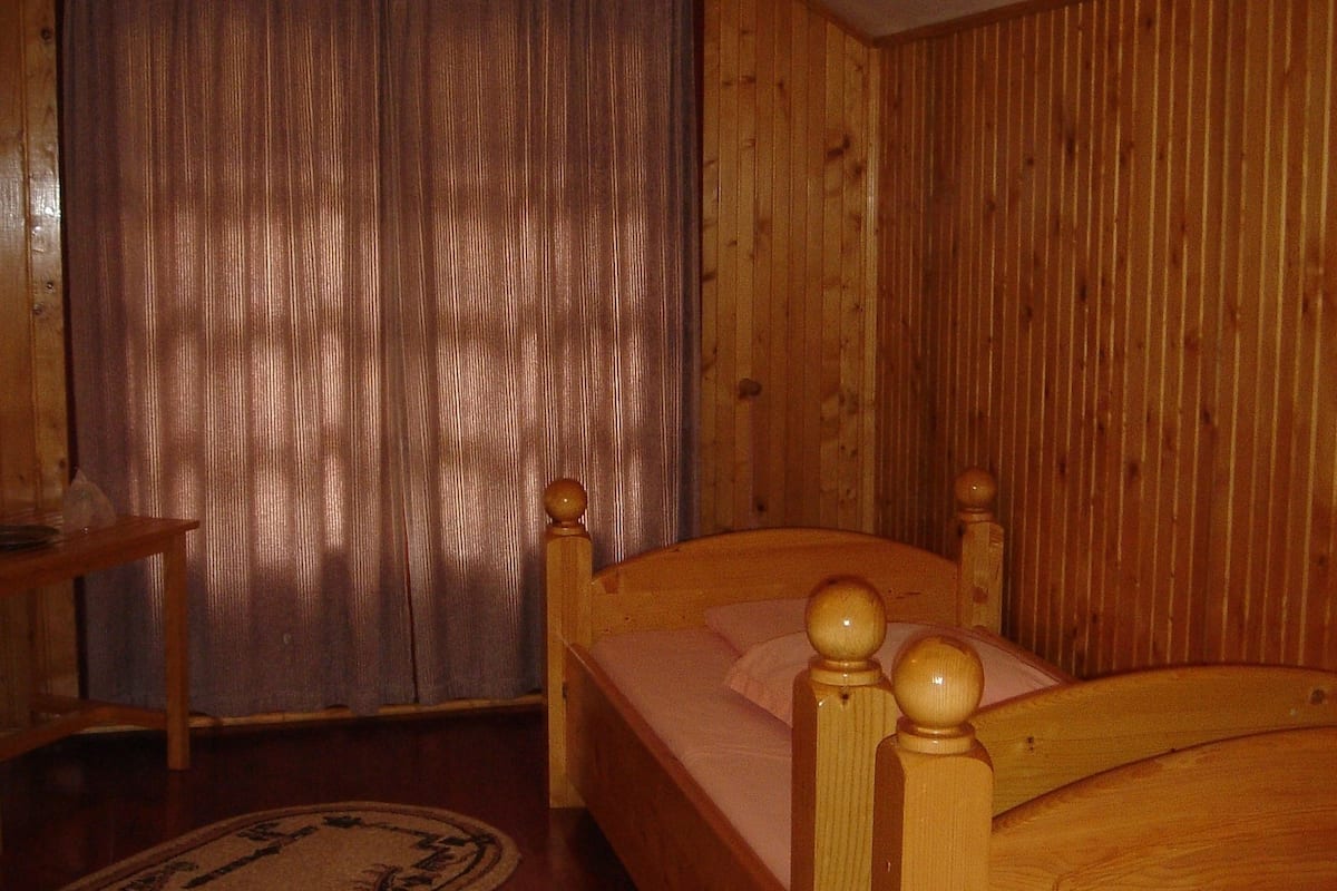 Ett rum med träpanel, en säng, en stol och en gardin.