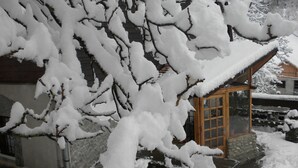 A snow-covered house with a wooden door and a stone wall. - Rem's Pension (Rasnov)