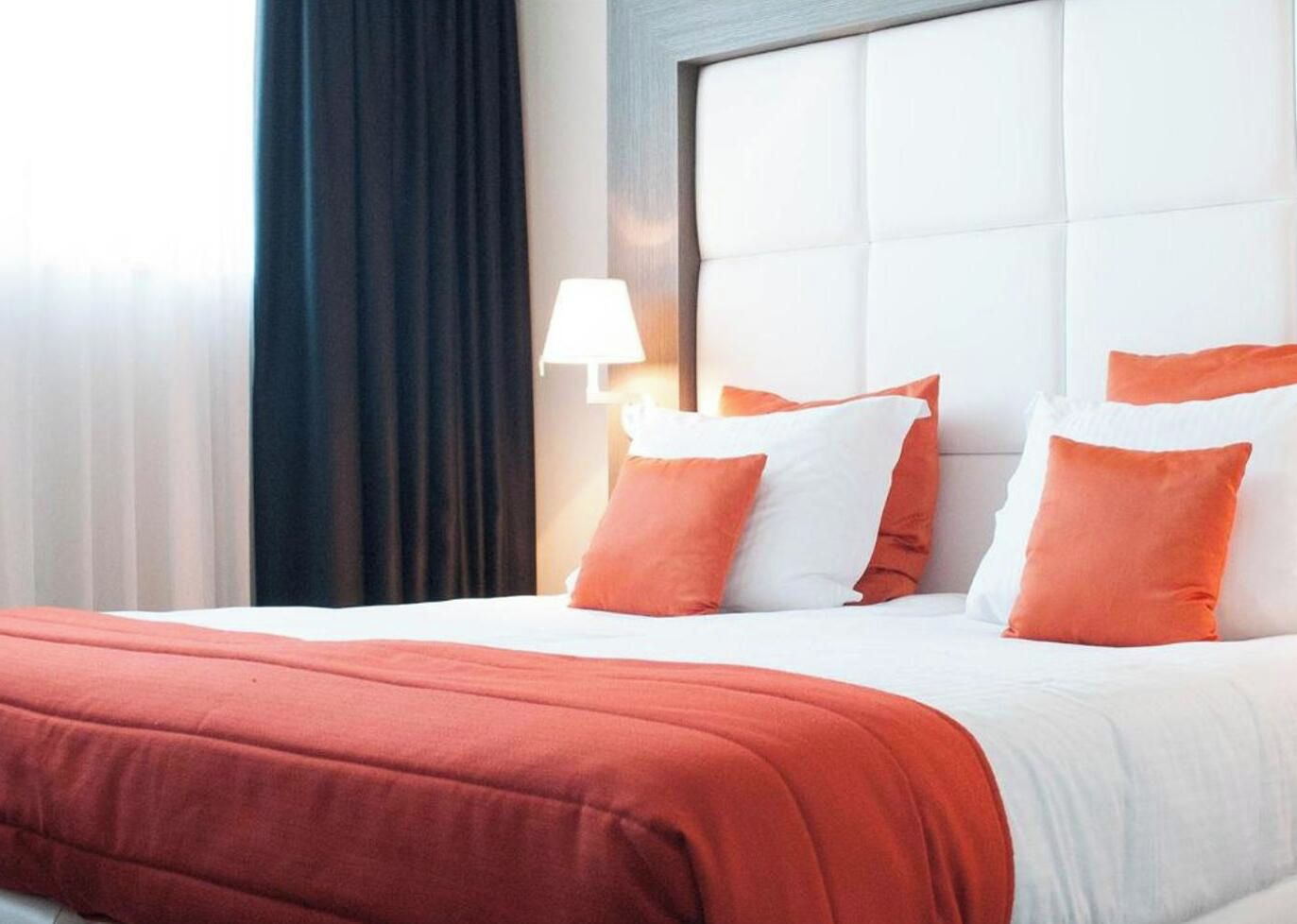 A hotel room with a bed, a headboard, and a nightstand with a lamp.