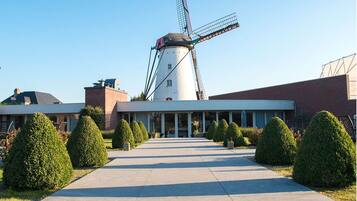 A modern building with a windmill, a paved walkway, and neatly trimmed bushes.