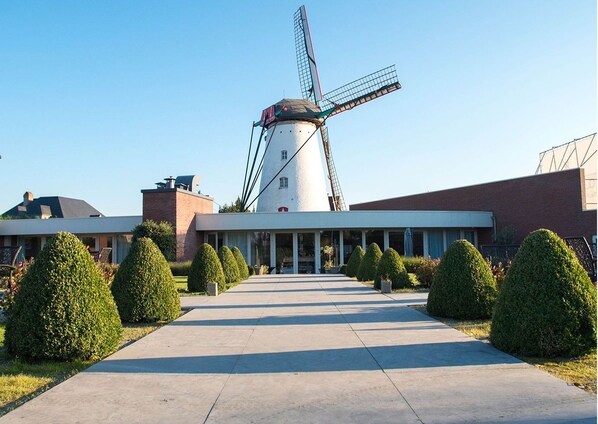 Un edificio moderno con un molino de viento, un camino pavimentado y arbustos bien cuidados.