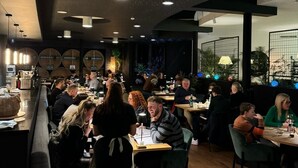 Un restaurante con una decoración moderna, que cuenta con una zona de bar con taburetes y mesas, y un techo con lámparas circulares.