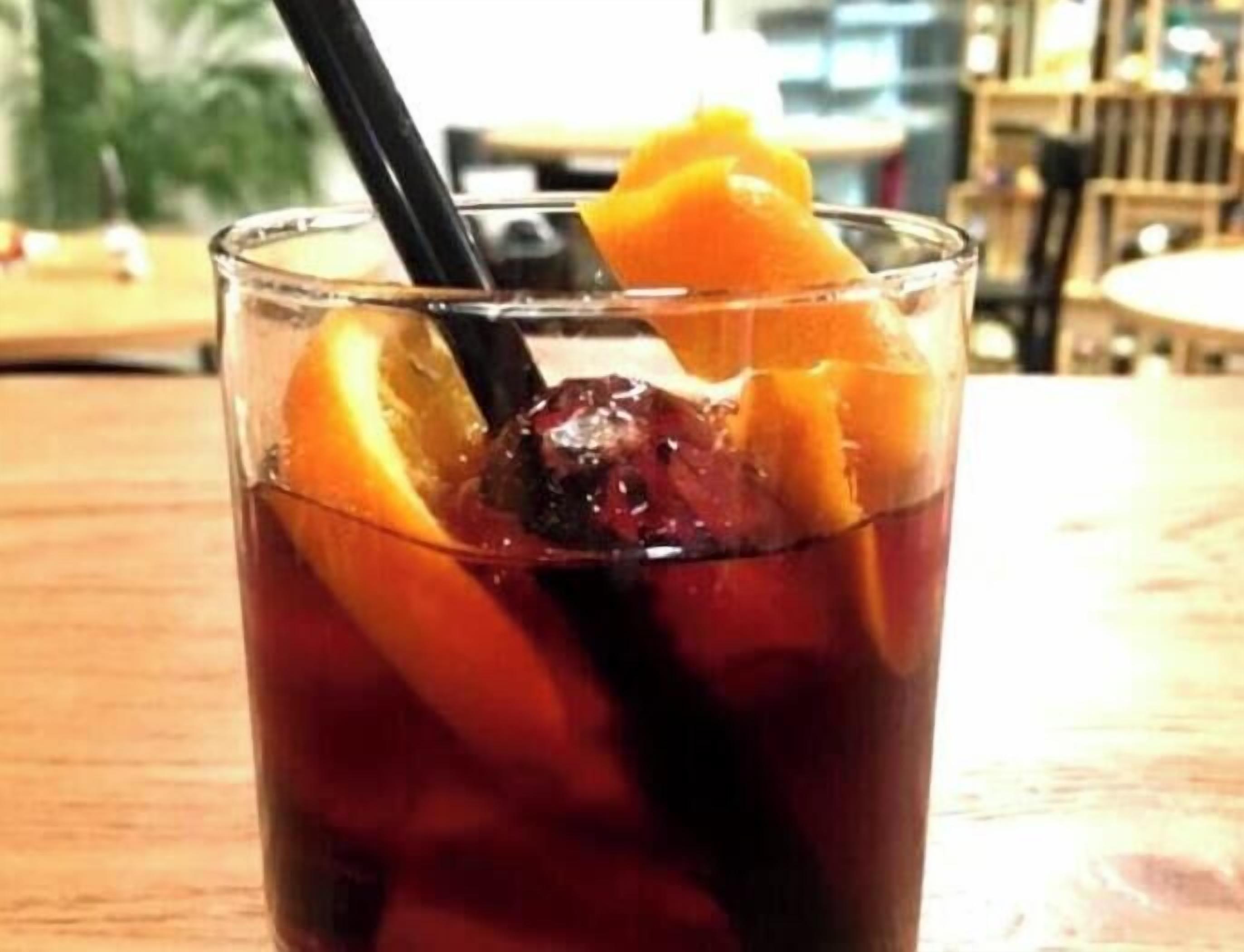 Un verre contenant un liquide foncé, des glaçons et une tranche d’orange.