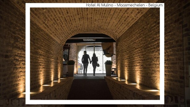 Un túnel de ladrillo que conduce a un vano con dos personas silueteadas contra la luz.