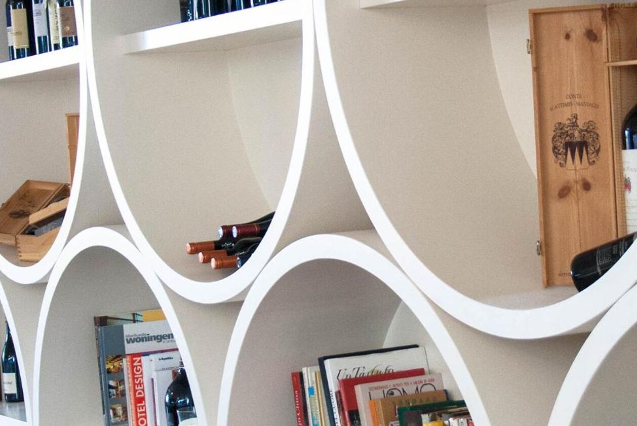 Ein modernes Hotelinterior mit weißen, geschwungenen Regaleinheiten, die Weinflaschen und Bücher präsentieren.