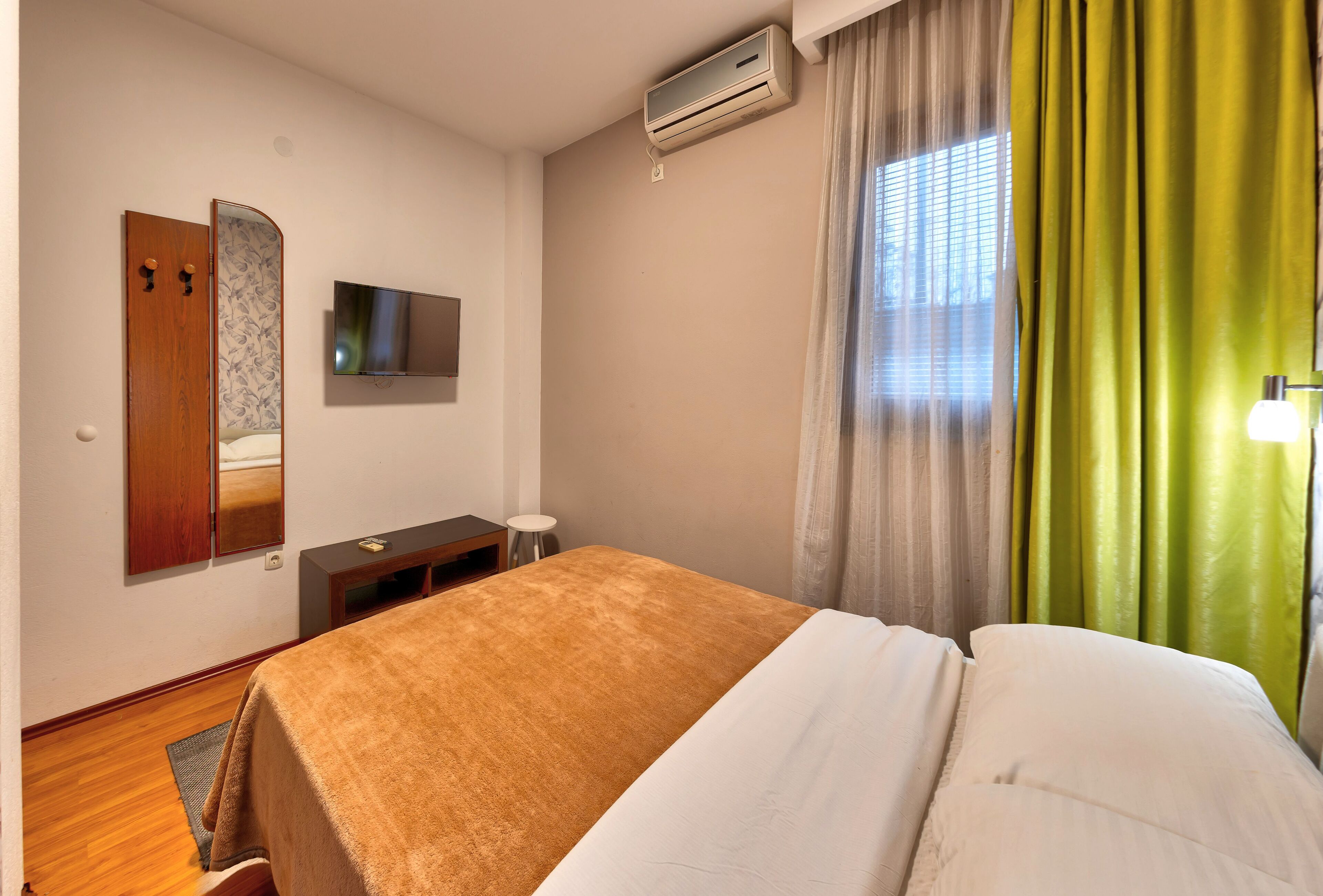 Una habitación de hotel con cama, televisión, aire acondicionado, espejo y ventana con cortinas.