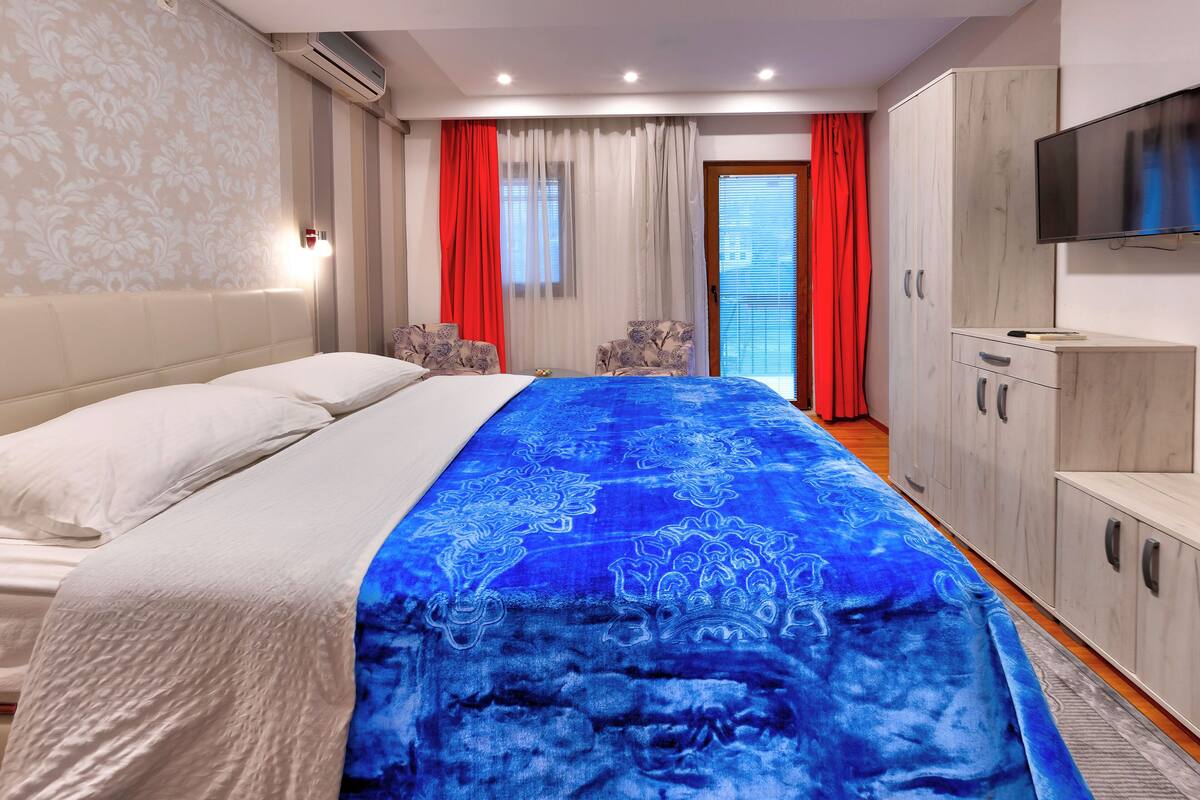 A hotel room with a bed, a TV, a wardrobe, and a window with curtains.