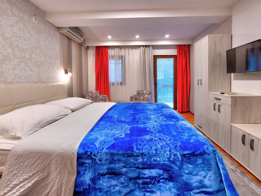 Une chambre d’hôtel avec un lit, une télévision, une armoire et une fenêtre avec des rideaux.