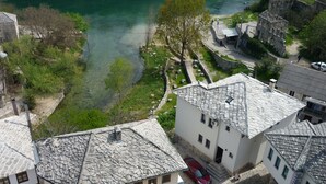 A traditional stone-roofed building with a courtyard, a river in the background, and parked cars.