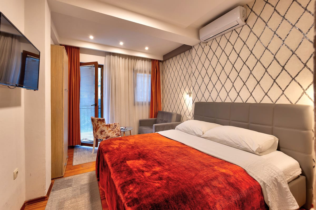 A hotel room with a bed, a desk, a chair, and an air conditioning unit.