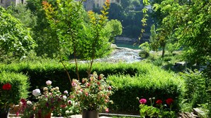A garden with a river, a stone building, and a church in the background.