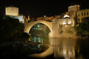 Un pont de pierre enjambant une rivière, avec des bâtiments et une tour de chaque côté.