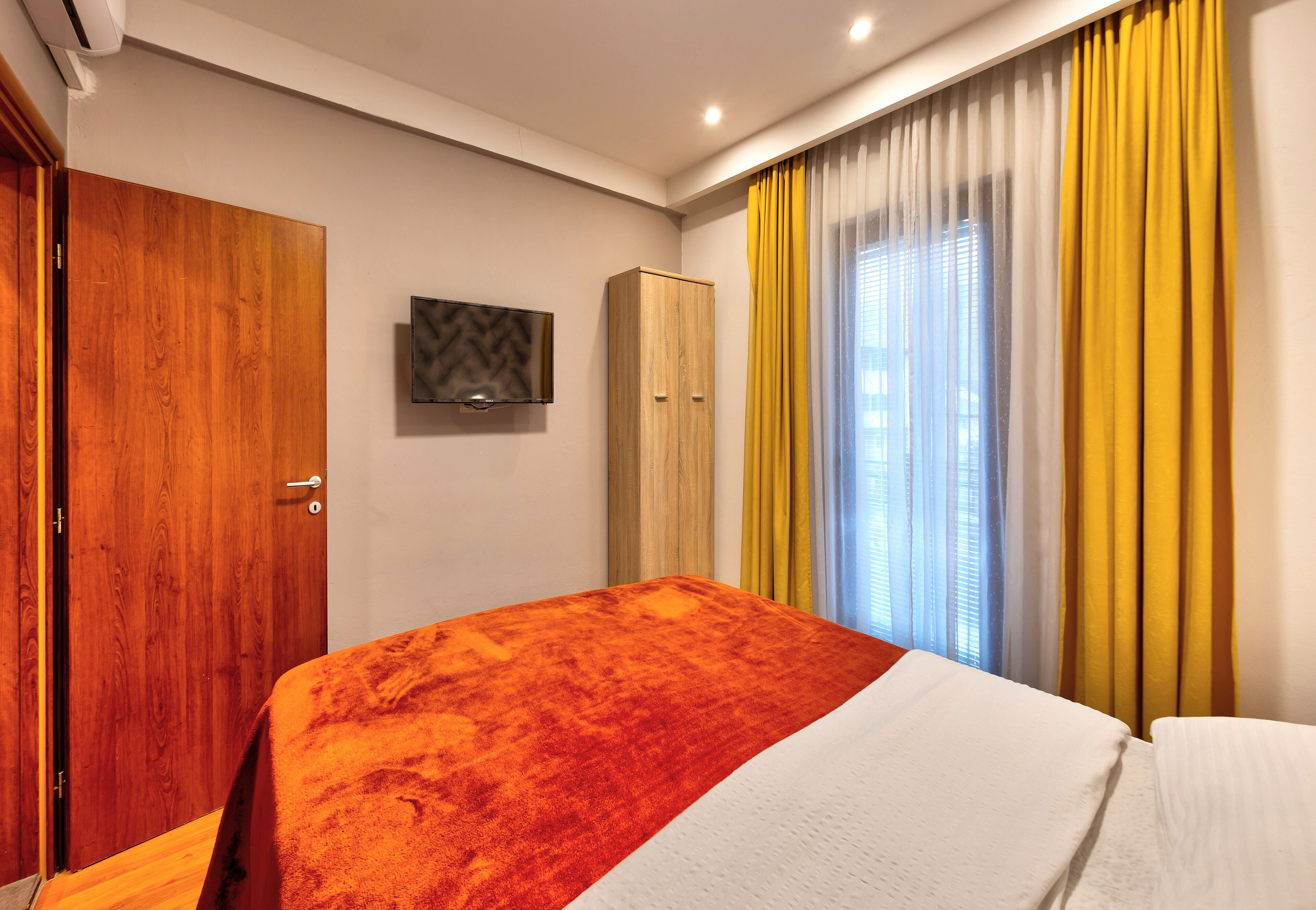 Una habitación de hotel con cama, armario, televisor y cortinas.