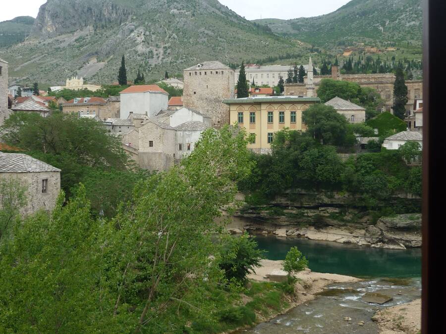 A town with historic buildings, a river, and mountains in the background.