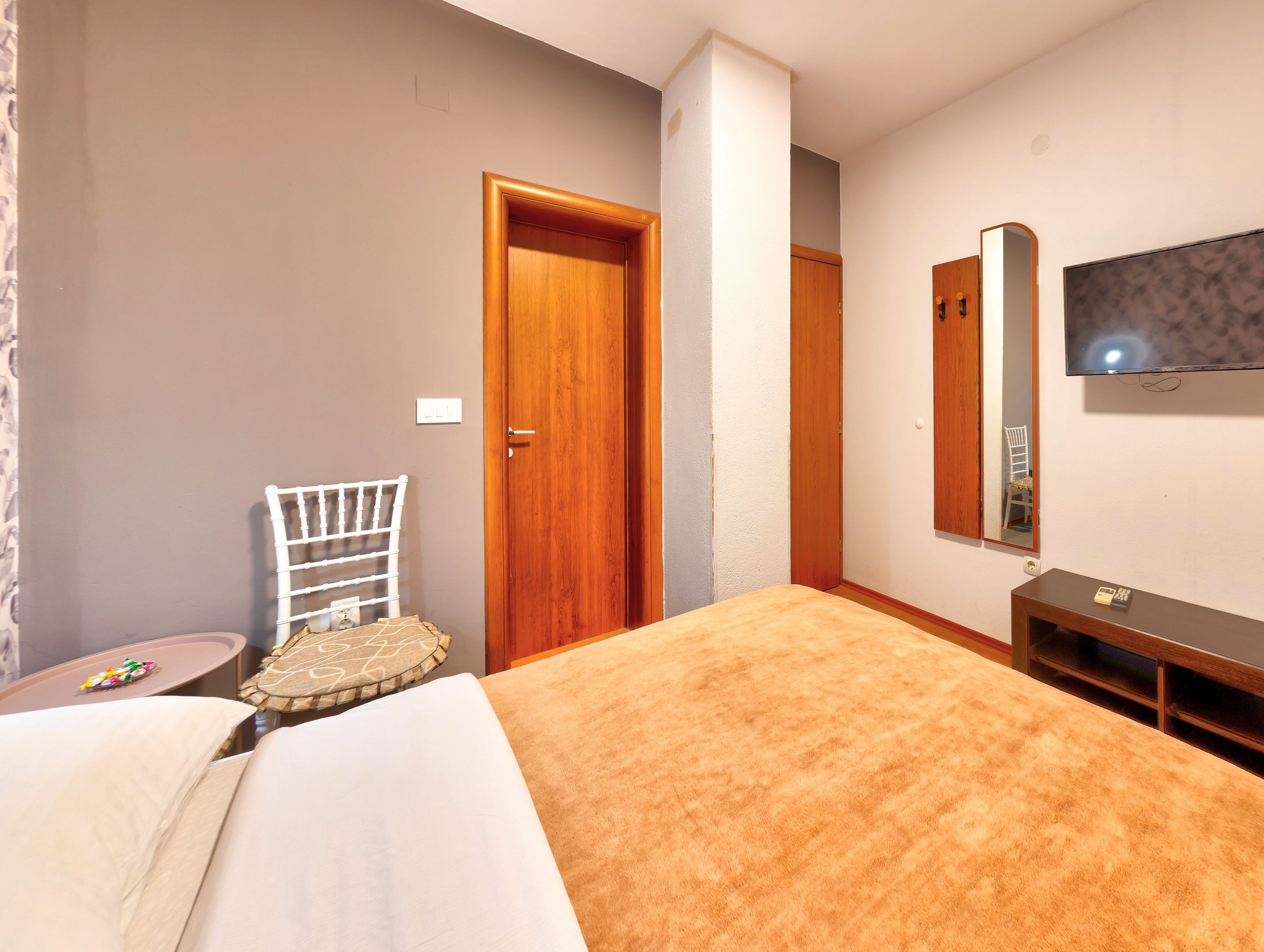 A bedroom with a bed, a chair, a TV, and a wooden door.