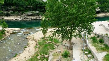 Une promenade au bord de la rivière, avec un revêtement de pavés, un arbre et une vue sur une ville où l’on aperçoit des bâtiments et une église en arrière-plan.