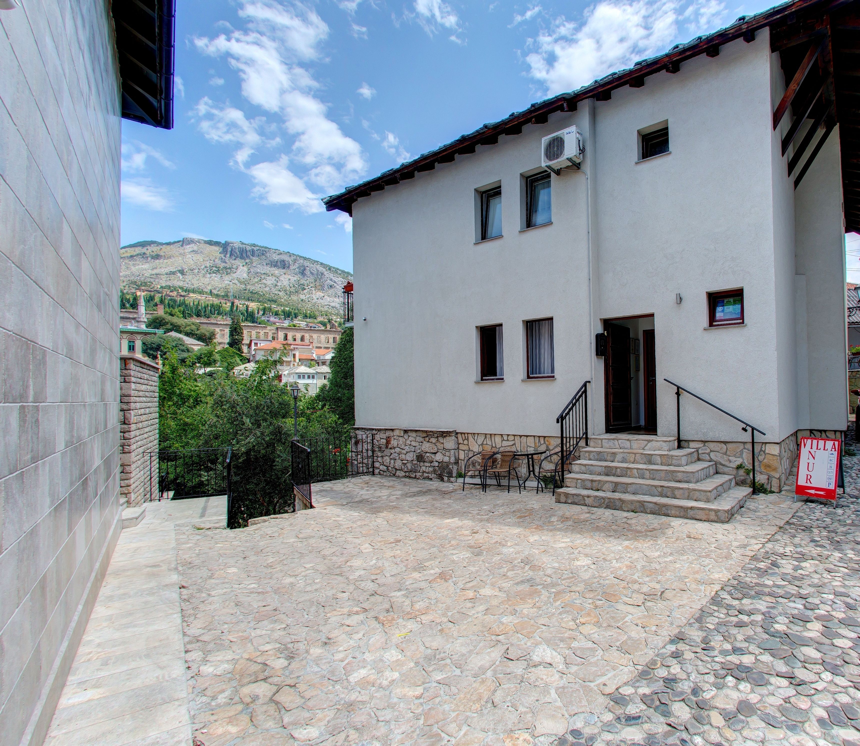 A building with a stone facade, a small outdoor seating area, and a view of a mountainous landscape in the background.