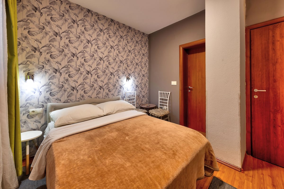 A bedroom with a bed, a small table, a chair, and a door.