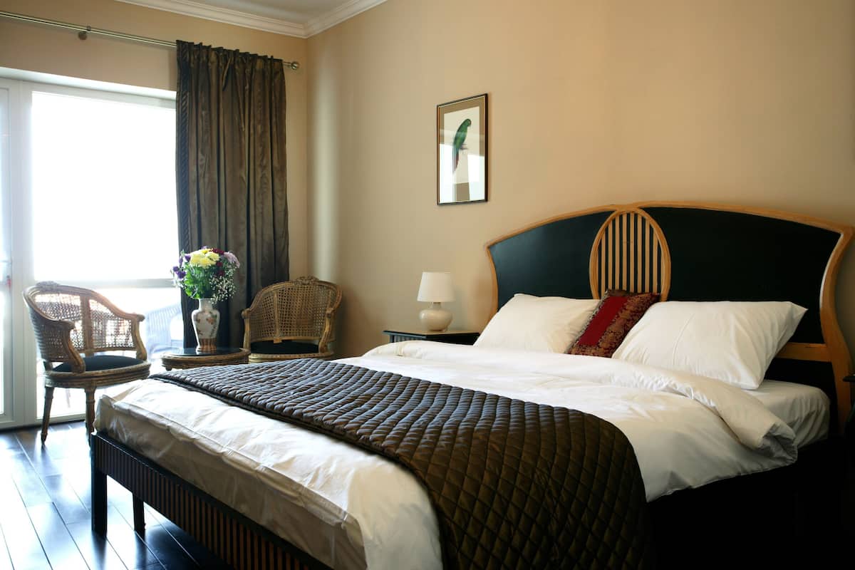 Une chambre d’hôtel avec un grand lit, une chaise, une table de chevet, une lampe et une fenêtre avec des rideaux.