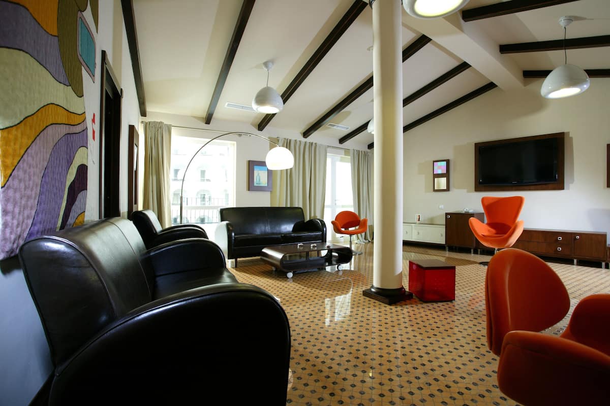 Un salon moderne avec un canapé noir, des fauteuils orange, un téléviseur et un sol à motifs.