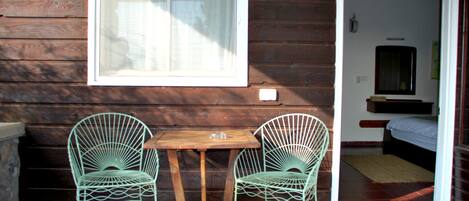 A wooden exterior wall with a window and two metal chairs with a wooden table.