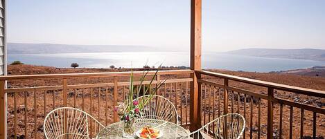 A wooden deck with a table and chairs overlooking a body of water and distant hills.
