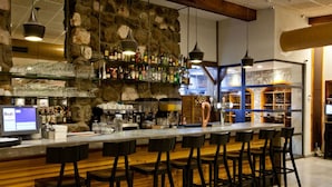 A bar area with a stone wall, bar stools, and a long counter with various bottles and glasses.