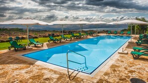 A swimming pool with lounge chairs and umbrellas, surrounded by a landscaped area with a view of distant hills.