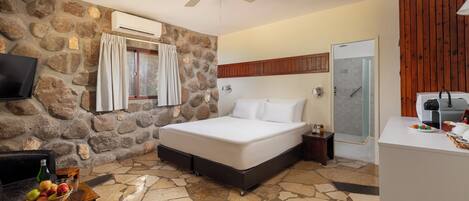 A bedroom with a stone wall, a bed, a TV, a ceiling fan, a shower, and a breakfast bar.