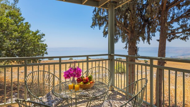 A balcony with a metal chair, a small table with fruit and flowers, and a view of the sea.