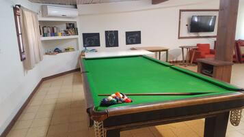 A pool table with balls, a bookshelf with books, and a television on the wall.