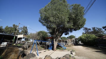 Un parque infantil con columpios y un tobogán, rodeado de rocas y árboles.
