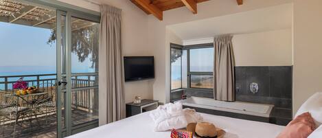Habitación de hotel con una cama grande, televisión, balcón con vistas al mar y techo de madera.